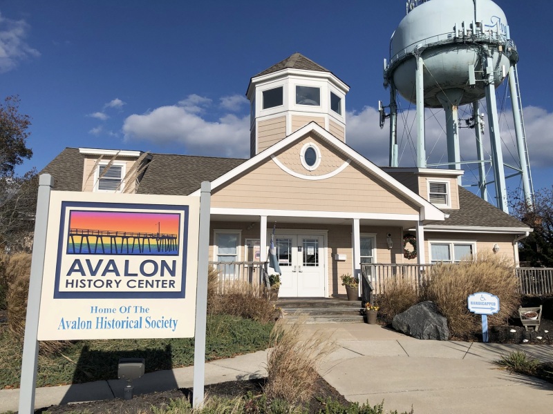 A color photo of the front of the Avalon History Center building at 215 39th St. Avalon NJ with the water tower in the background and the Avalon History Center sign in the foreground