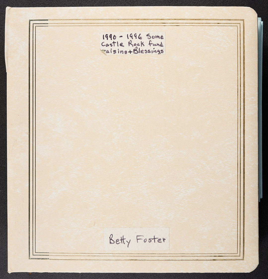 A cream colored photograph album cover with cold tooling bordering the edges. Written on white tape adhered to the top and bottom is, "1990-1996 Some Castle Rock fund raising & blessings" and "Betty Foster."