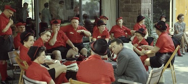 Vintage color photograph of alumni or campus visitors at an event, wearing matching bright red shirts and coordinated hats while socializing on an outdoor patio.