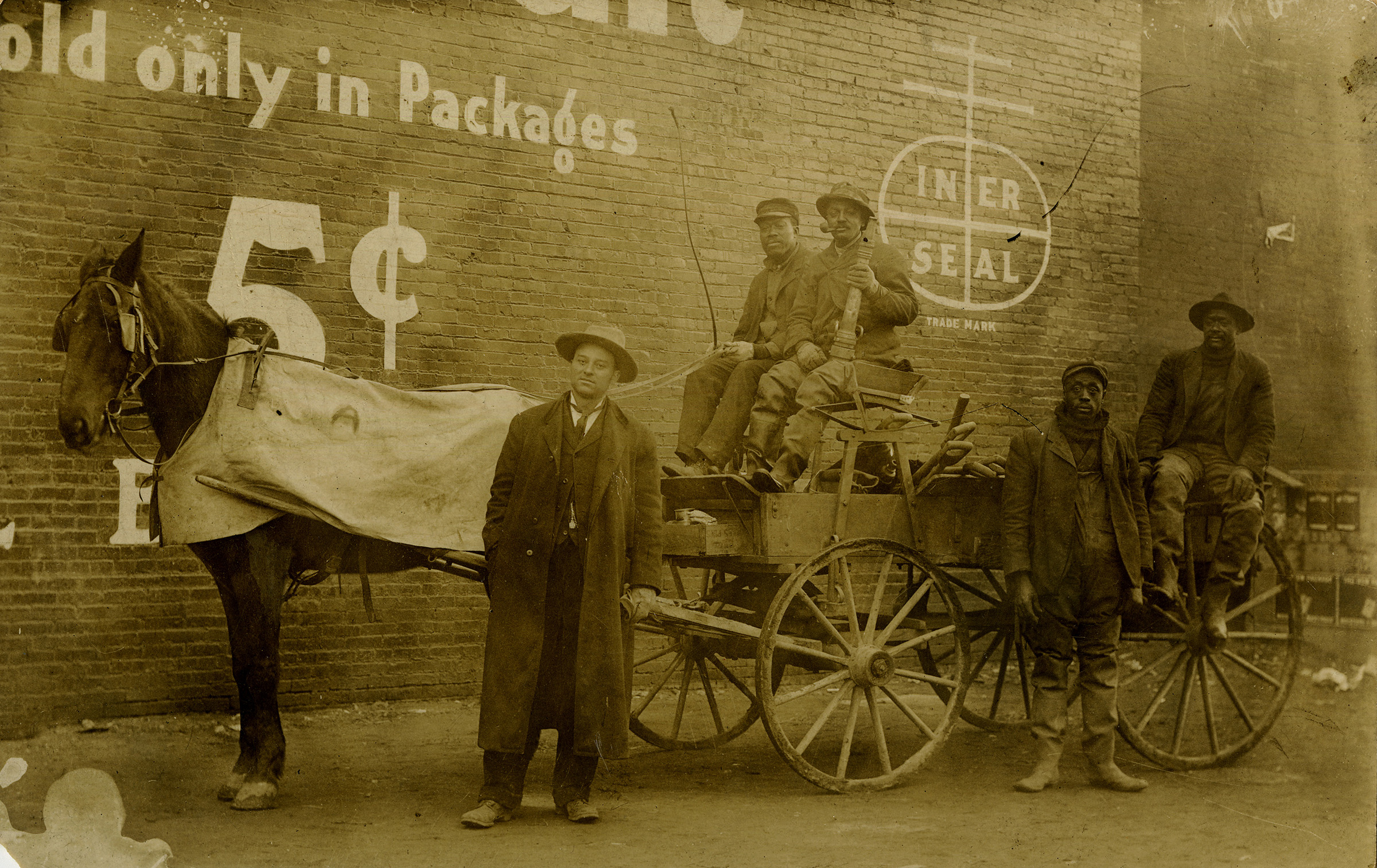 A horsedrawn wagon with people sitting and standing on it or around it.