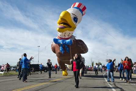 people marching in a parade holding a large, inflatable bird with ropes
