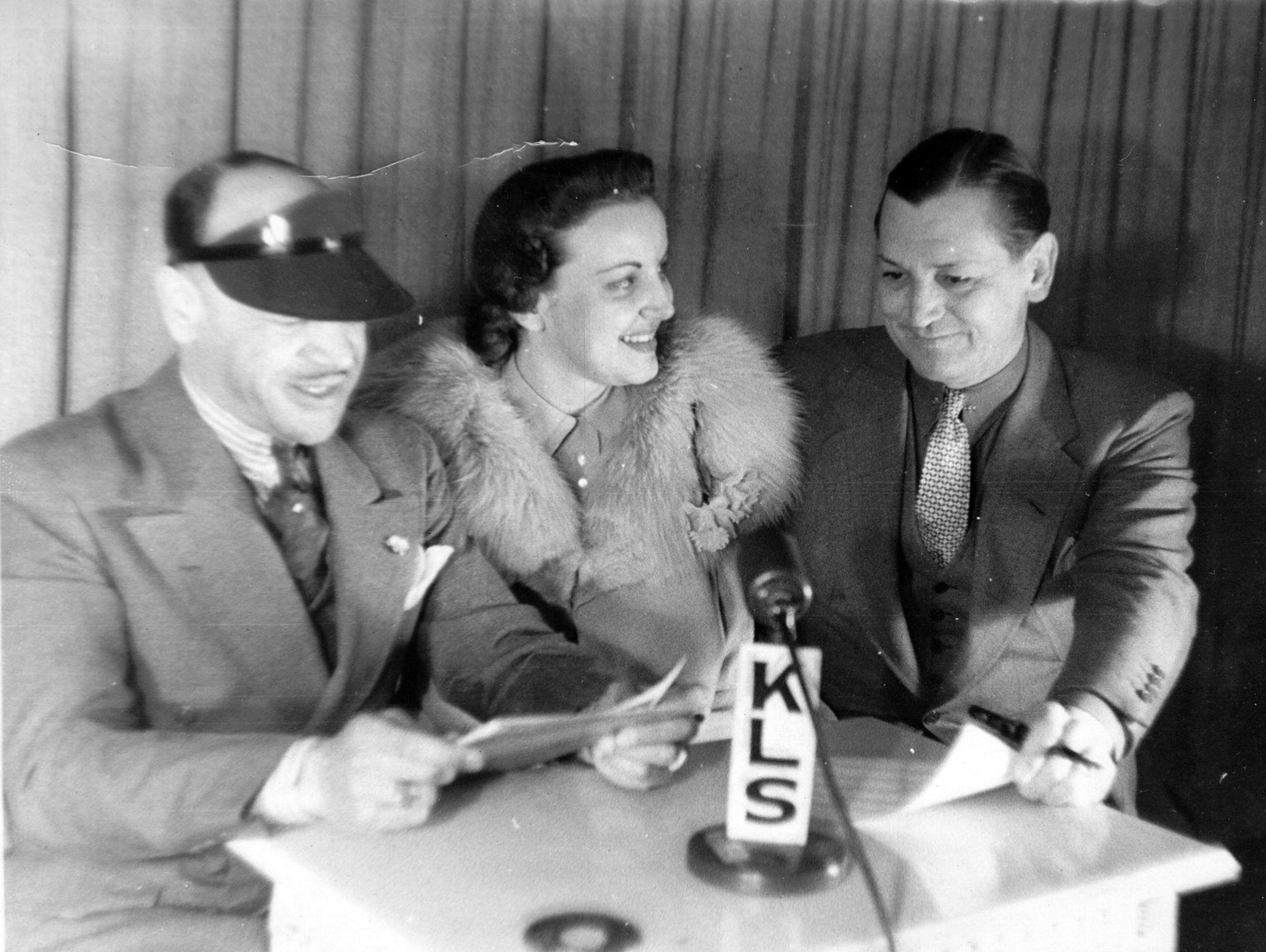Two men and three women sitting at a table in front of a microphone