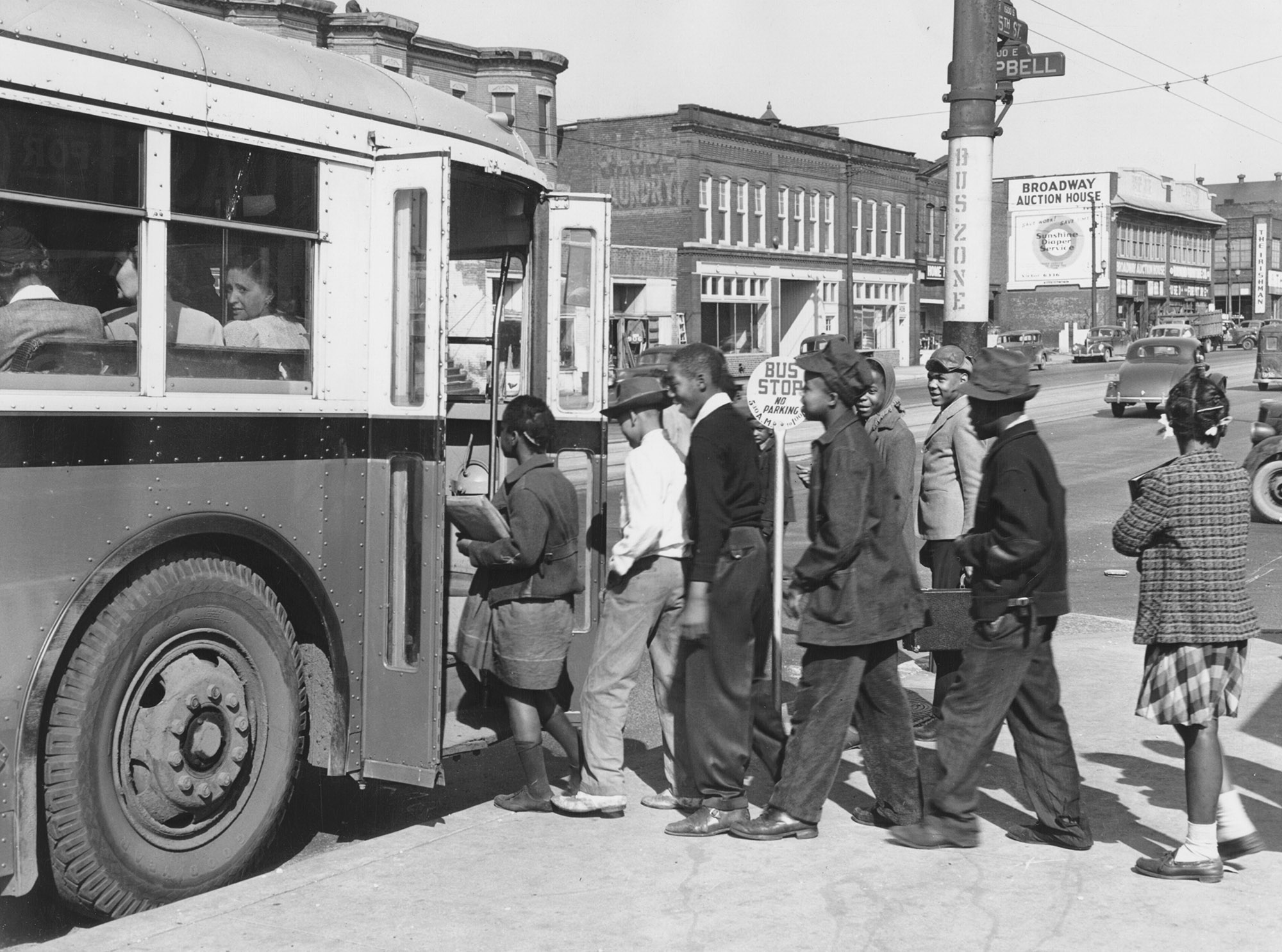 A group of people waiting to board a bus which waits on the street
