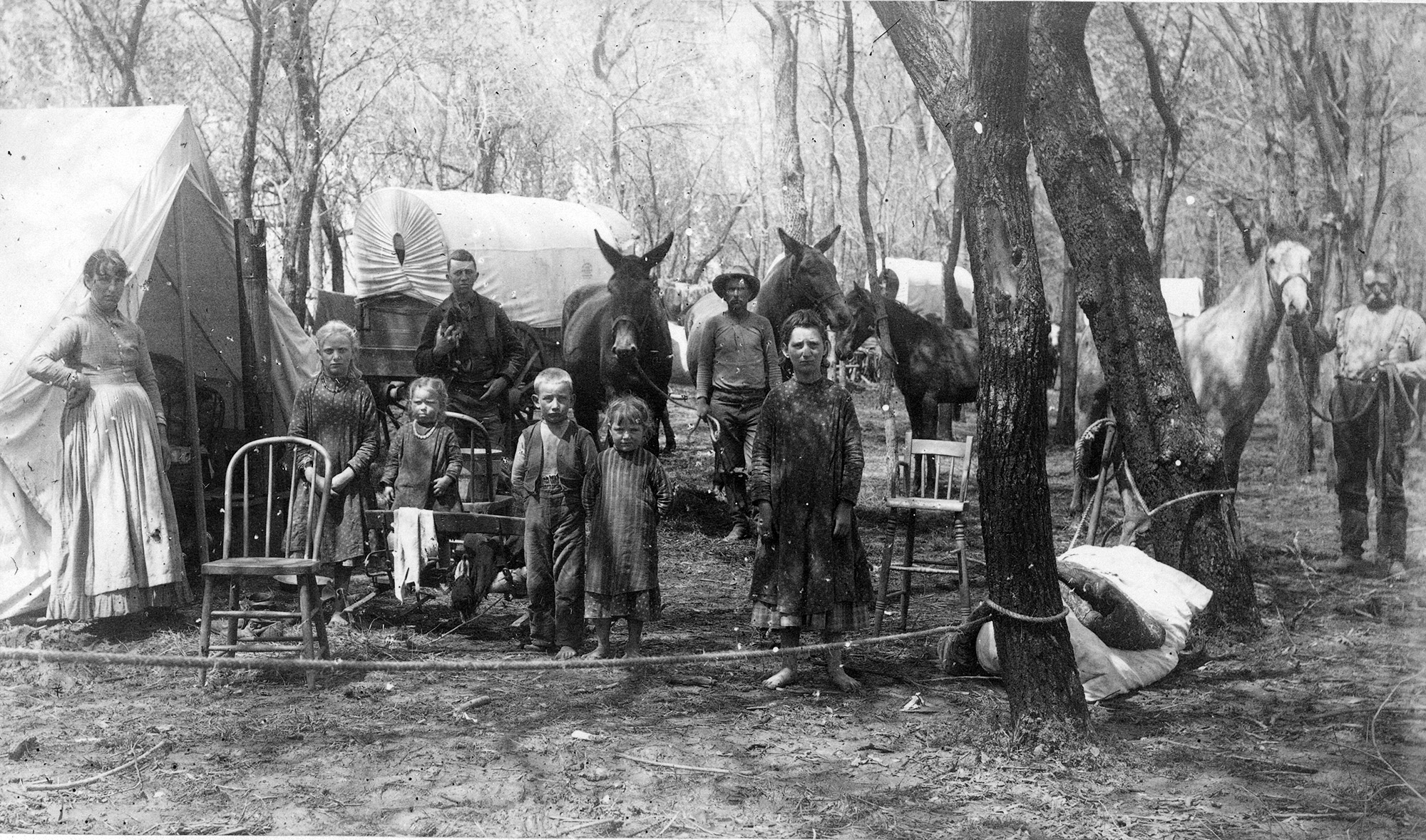 A family posing with tents, covered wagons, chairs and horses in view.