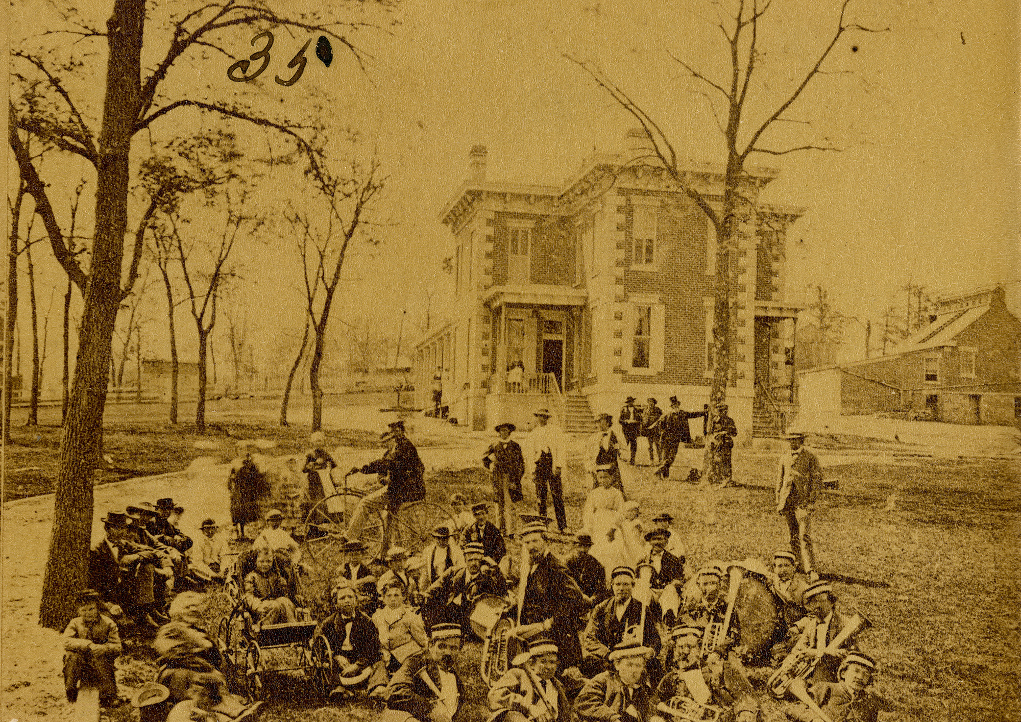 A group of people seated outside with a house visible in the background.