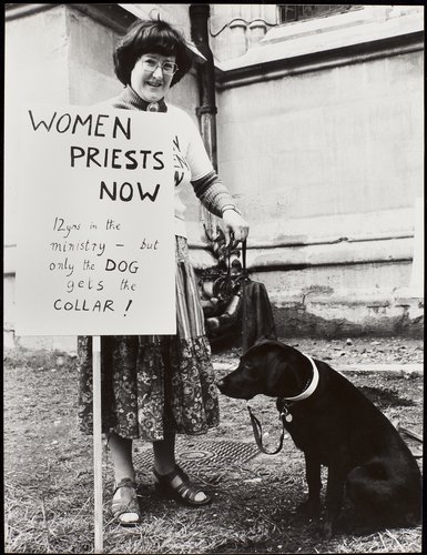 A woman holding a placard with a dog sitting next to her.