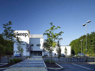 The Keep in Brighton. It is a simple, flat-roofed white building in a modern architectural style, with a tree-lined car park in front.