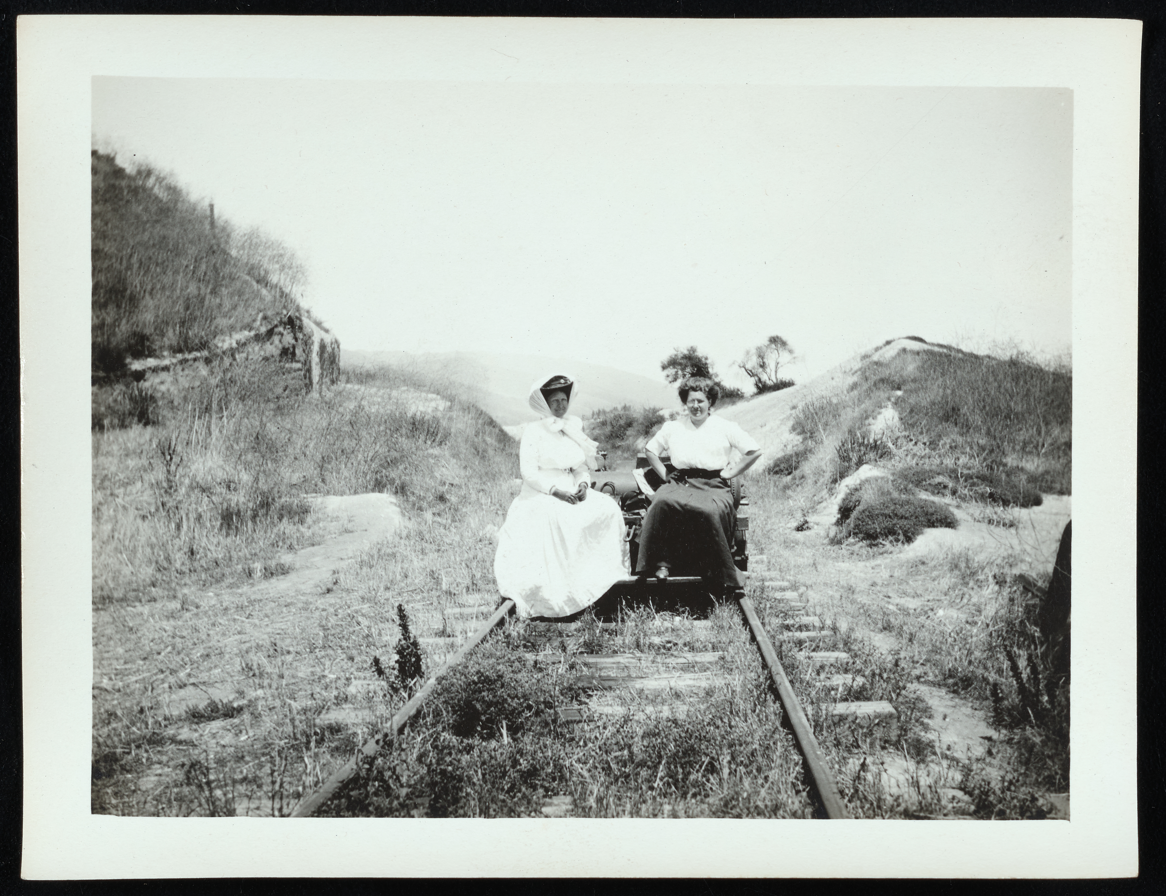 Two women, Rhoda Agatha Rindge and Rhoda May Rindge, sitting on a railroad handcar together with a malibu valley in the background