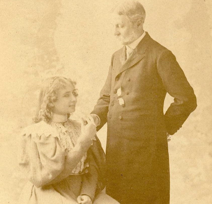 Studio portrait of Helen Keller with Mr. Arthur Gilman. Keller is seated and Gilman stands. He is fingerspelling into her hand
