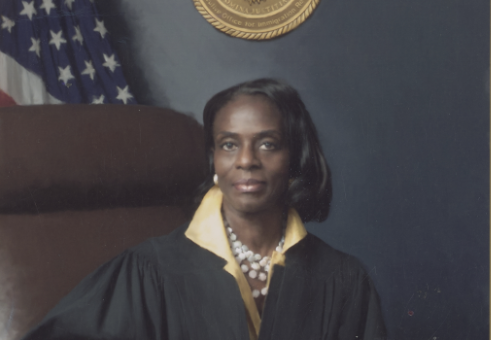 Judge Clarease Yates in judges robes sitting in a leather chair in front of the American flag.