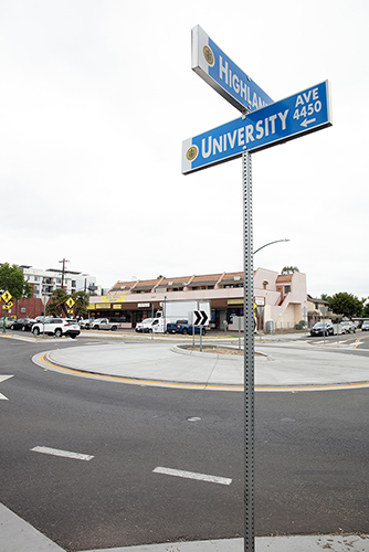 A color image of a street sign in front of a round-a-bout.