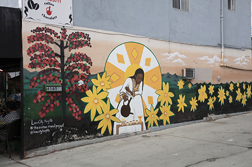 A color photograph of a mural depicting a woman pouring coffee in a field of flowers.