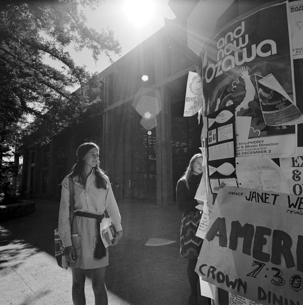 Black & white photo of student on campus adjacent to a light pole