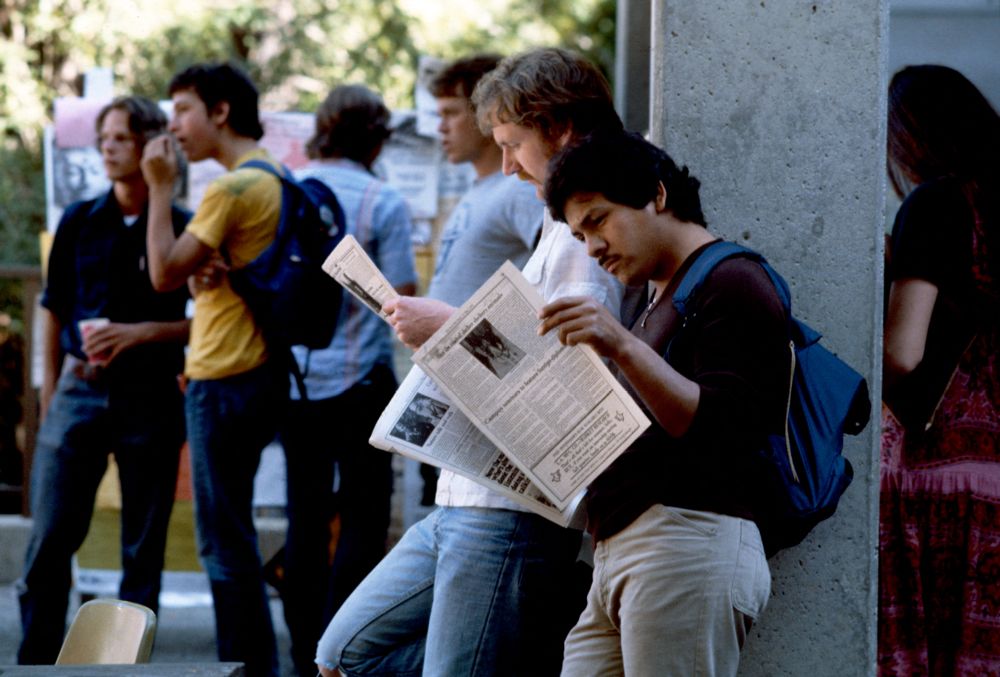 students reading newspapers outside a building on campus