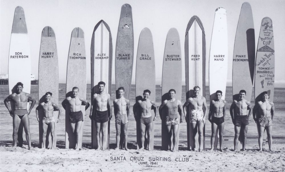 Surfers standing on the beach in front of their surf boards.