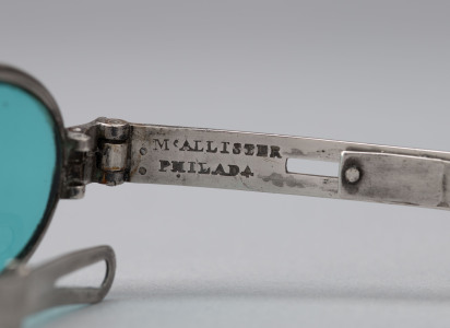 Detail photograph of "McAllister Philada" maker's mark stamped on spectacles's silver left arm.
