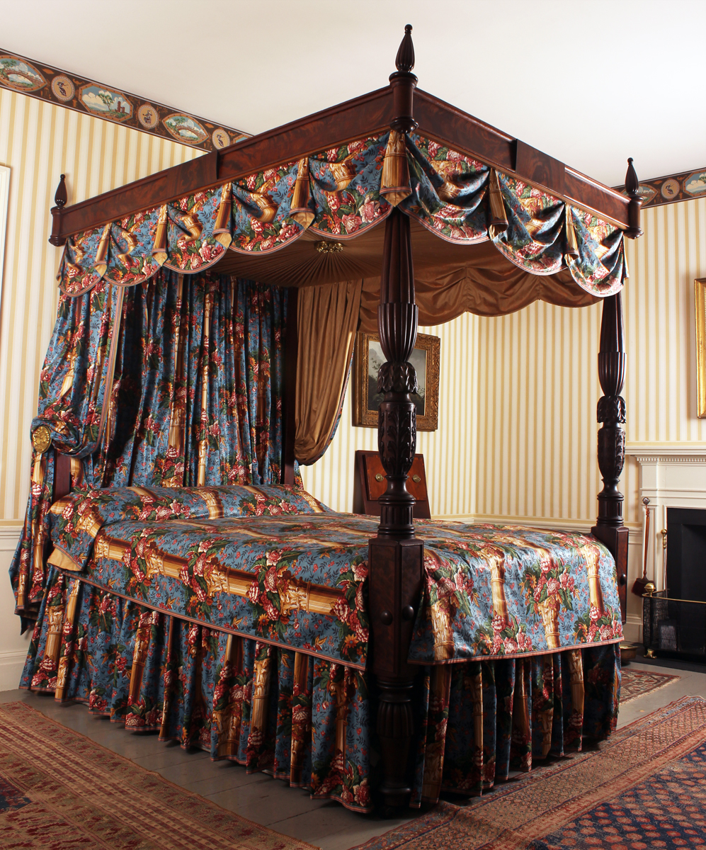 Photograph of a four-poster bed with multicolored bed coverings and curtains.